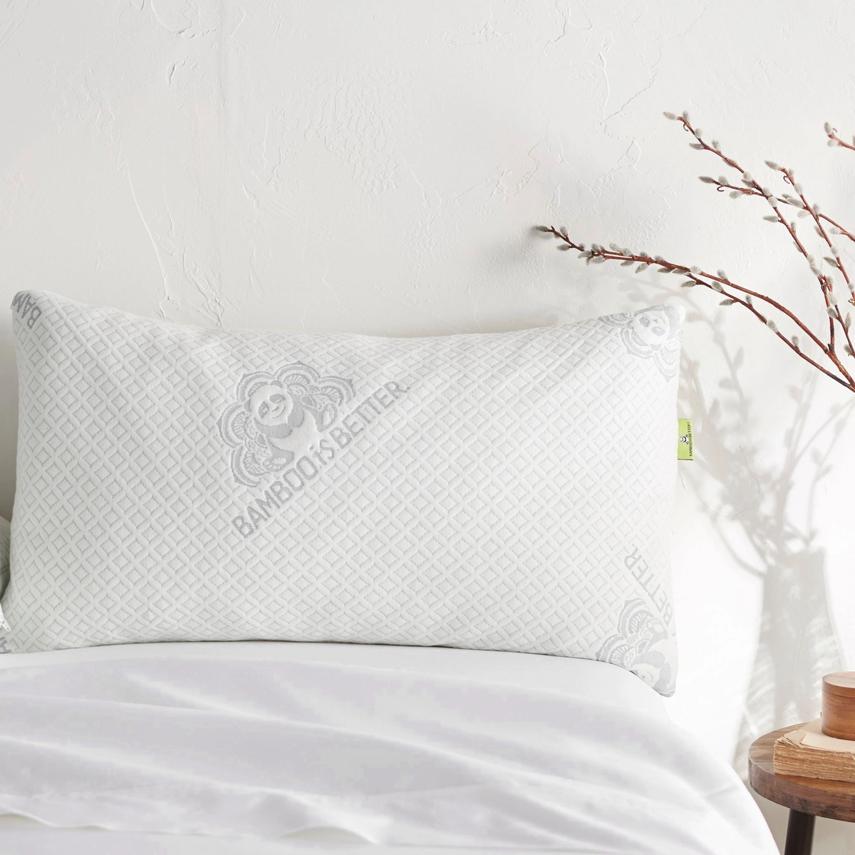Adjustable bamboo cooling pillow on a white bed with a branch in the background